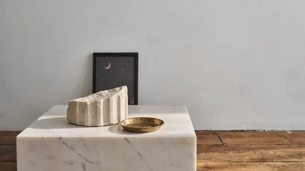 Marble plinth with a classical plaster fragment and a framed crescent moon print against a plaster wall