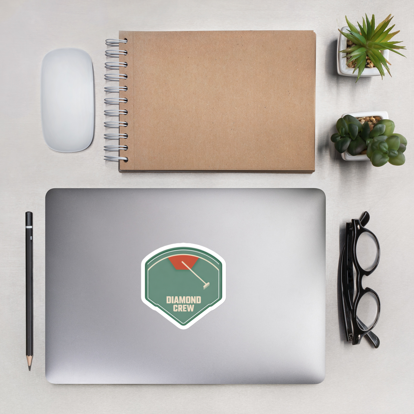 DIAMOND CREW 4 inch baseball sticker on a laptop in an overhead indoor desk with laptop, notebook, mouse, glasses and plants. Styling props are not included.