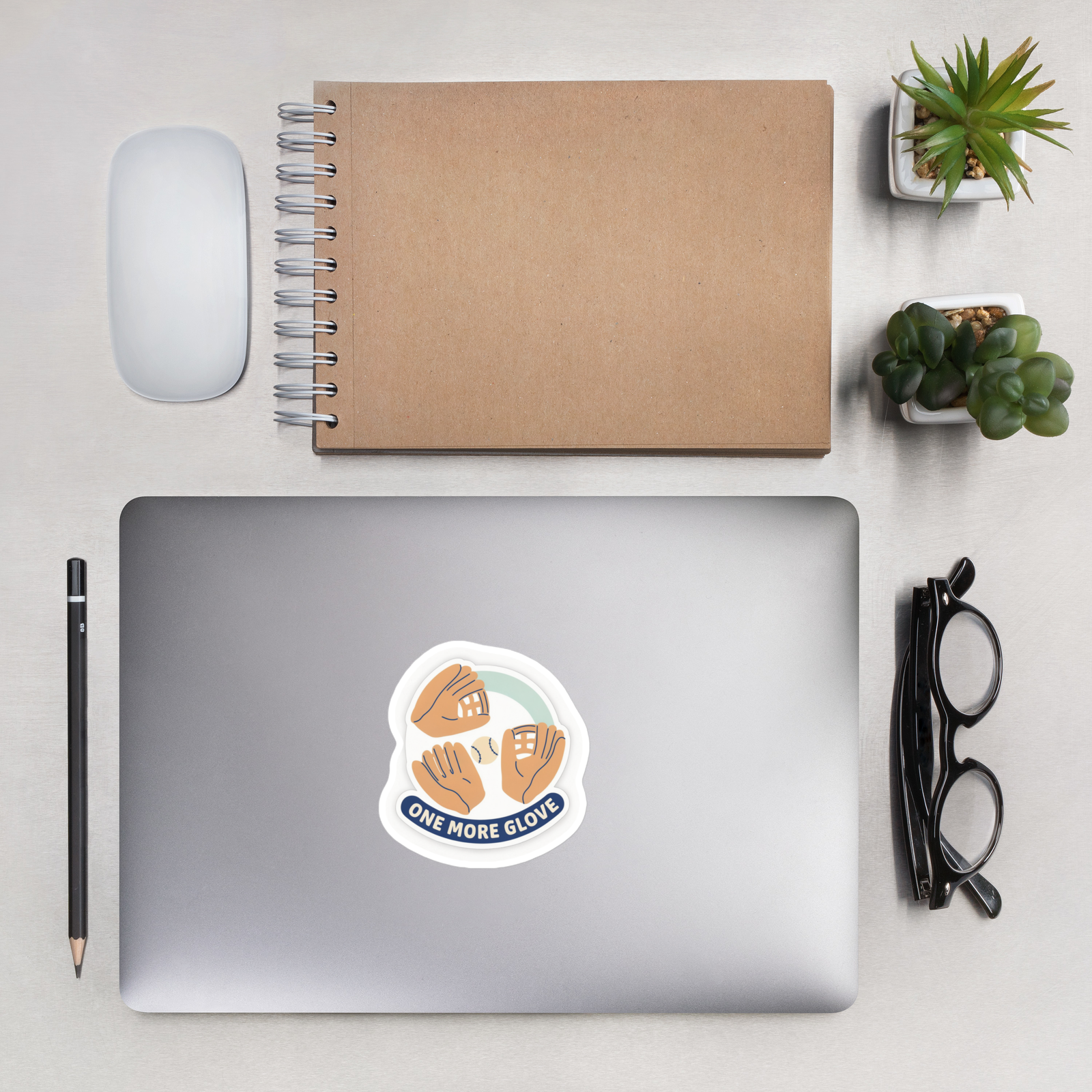 ONE MORE GLOVE 4 inch baseball sticker on a laptop in an overhead indoor desk with laptop, notebook, mouse, glasses and plants. Styling props are not included.