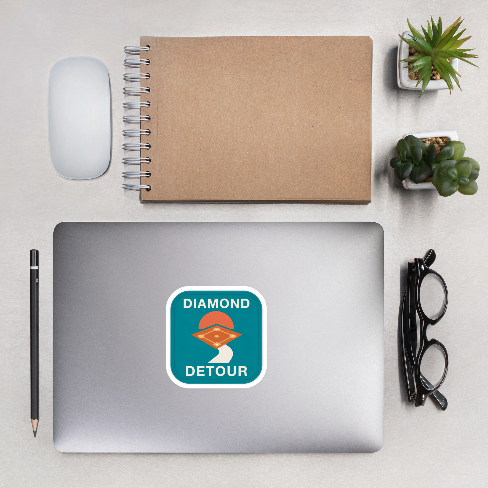 DIAMOND DETOUR 4 inch baseball sticker on a laptop in an overhead indoor desk with laptop, notebook, mouse, glasses and plants. Styling props are not included.