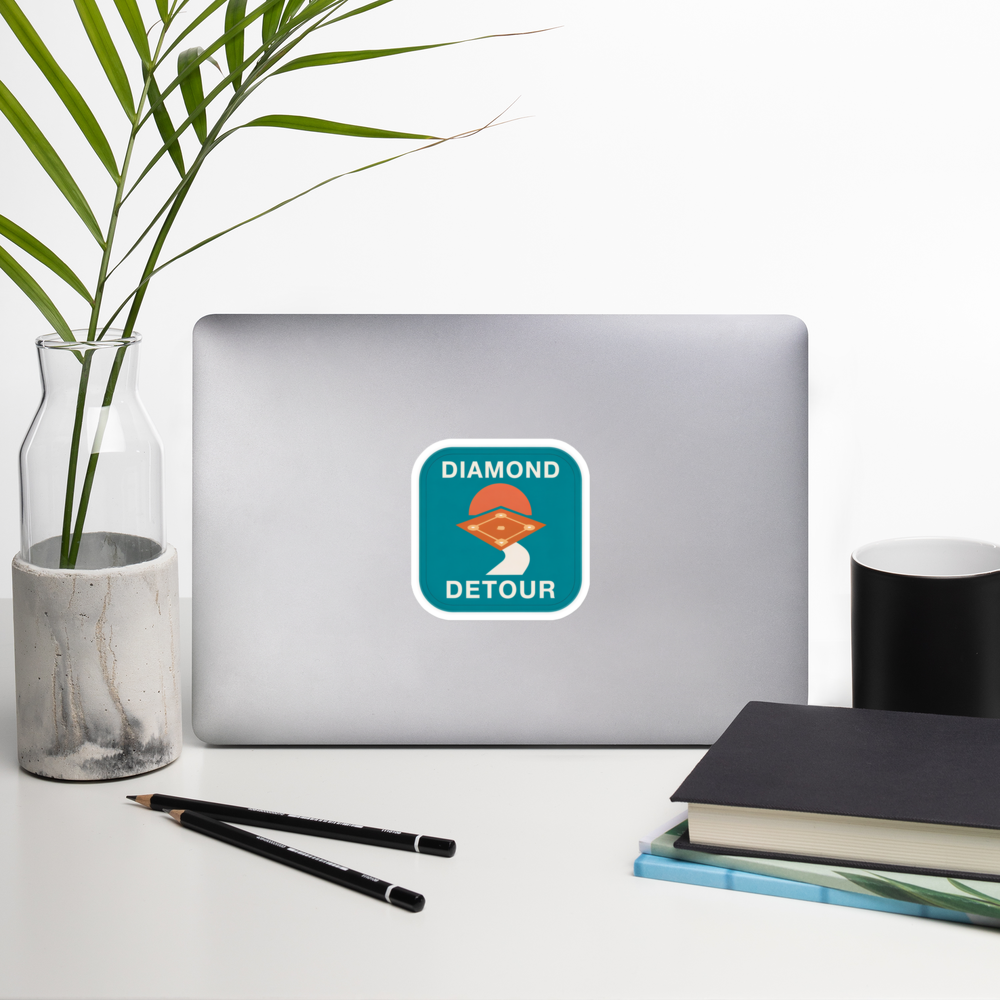 DIAMOND DETOUR 4 inch baseball sticker on a laptop in a front-facing indoor desk scene with books, a mug and a plant. Styling props are not included.