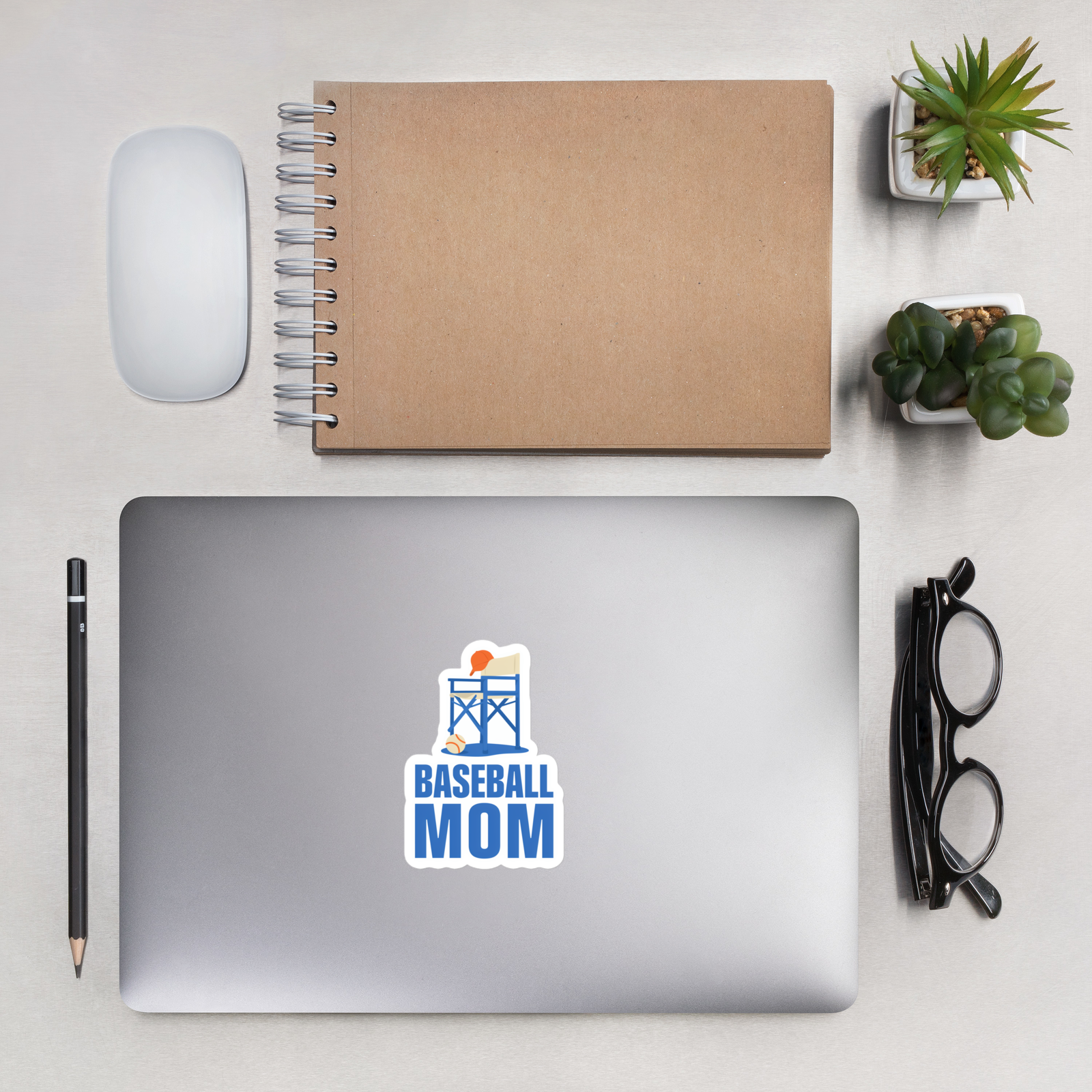 BASEBALL MOM 4 inch baseball sticker on a laptop in an overhead indoor desk with laptop, notebook, mouse, glasses and plants. Styling props are not included.
