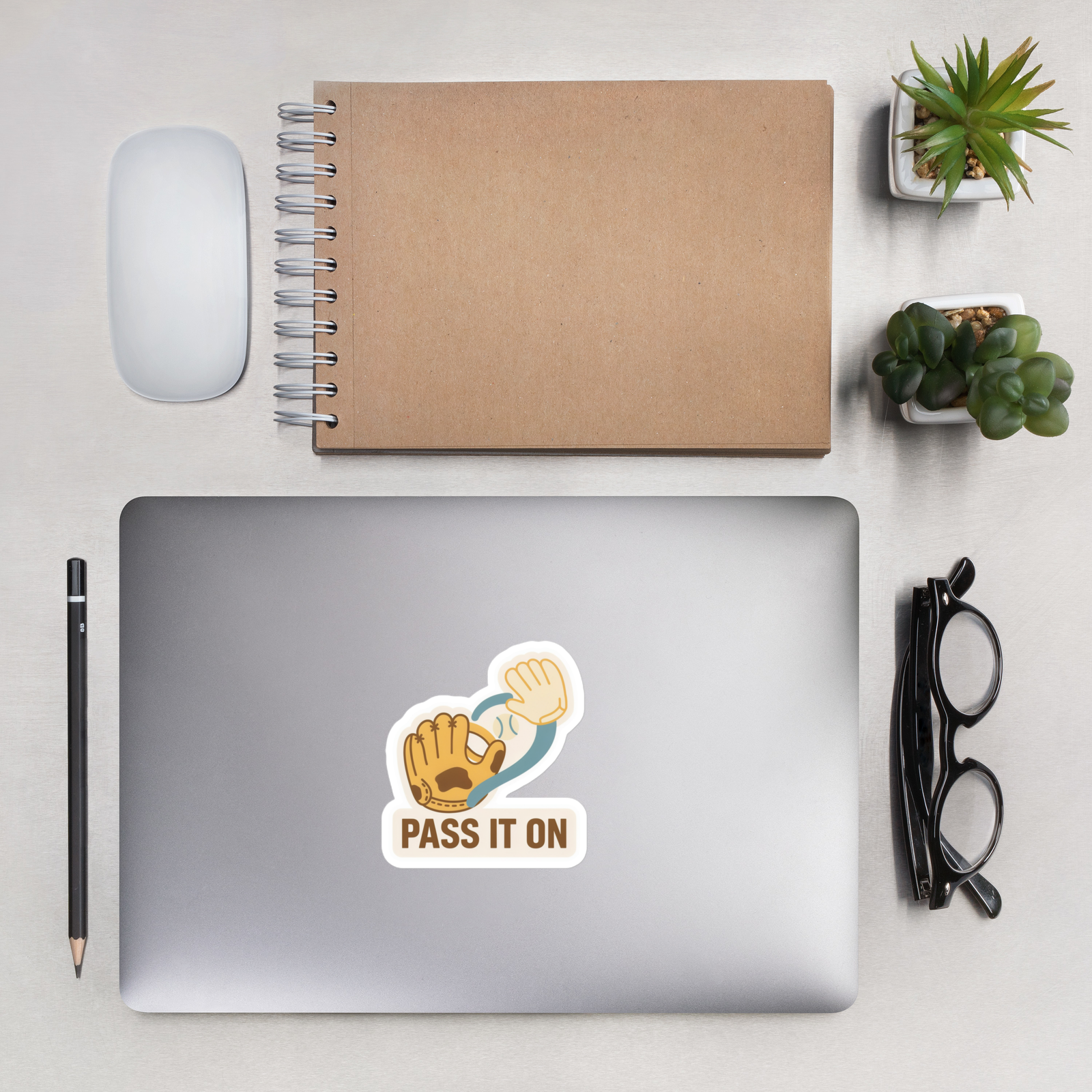 PASS IT ON 4 inch baseball sticker on a laptop in an overhead indoor desk with laptop, notebook, mouse, glasses and plants. Styling props are not included.