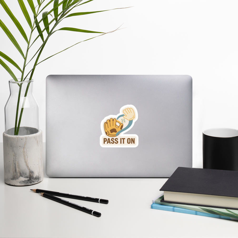 PASS IT ON 4 inch baseball sticker on a laptop in a front-facing indoor desk scene with books, a mug and a plant. Styling props are not included.