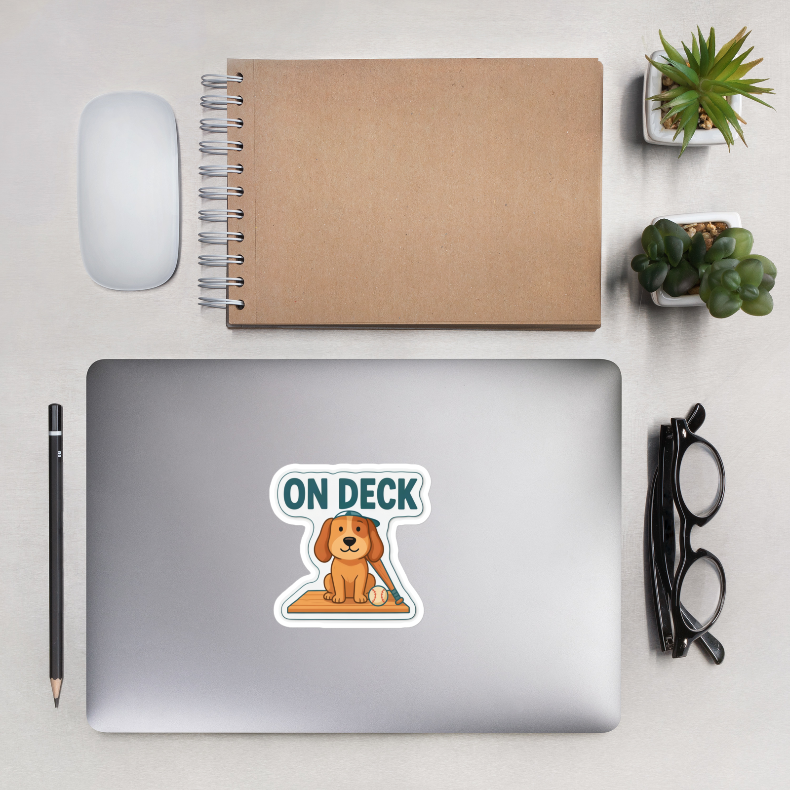 ON DECK 4 inch baseball sticker on a laptop in an overhead indoor desk with laptop, notebook, mouse, glasses and plants. Styling props are not included.