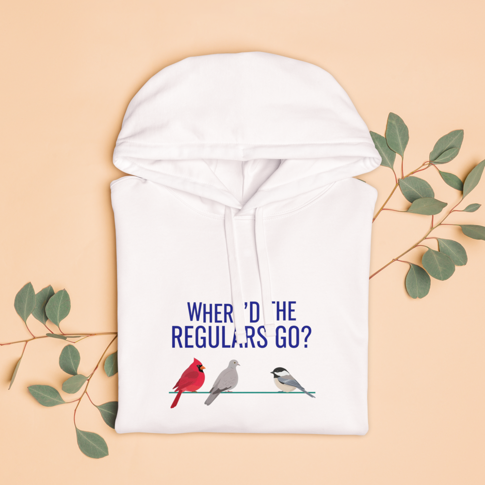 The white backyard bird hoodie folded with eucalyptus leaves, showing WHERE'D THE REGULARS GO? above three birds with a gap