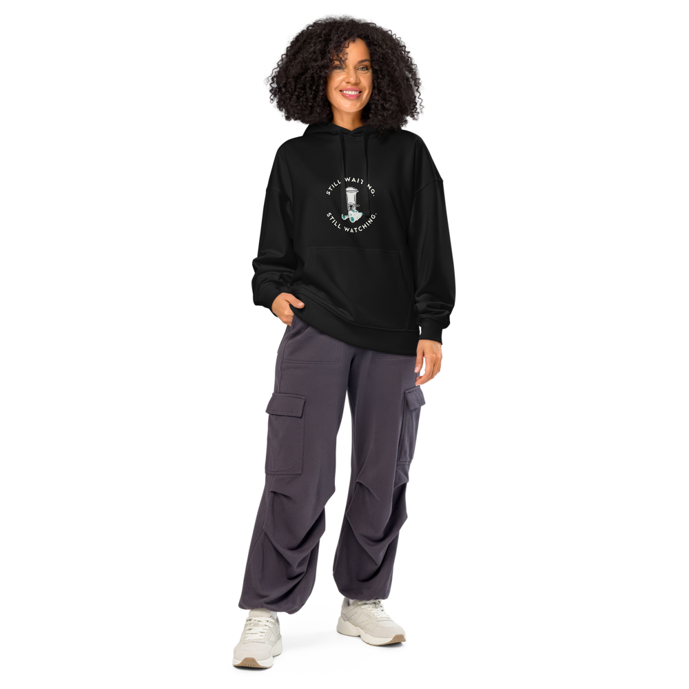 Woman wearing the black bird hoodie with STILL WAITING. STILL WATCHING. around a feeder and binoculars