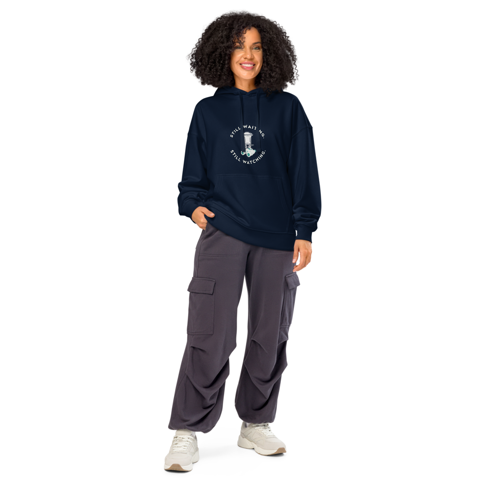 Woman wearing the French Navy bird hoodie with STILL WAITING. STILL WATCHING. around a feeder and binoculars