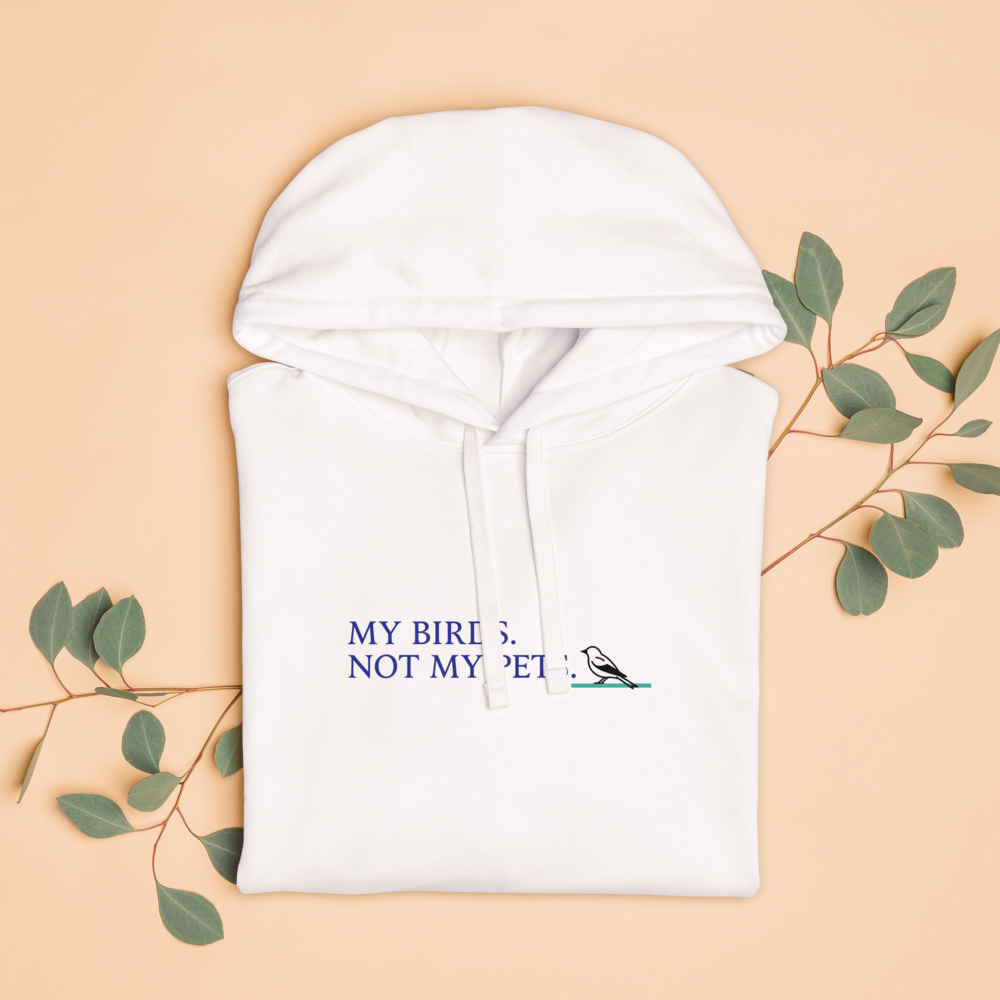 The white bird lady hoodie folded with eucalyptus leaves, showing MY BIRDS. NOT MY PETS. with a small songbird