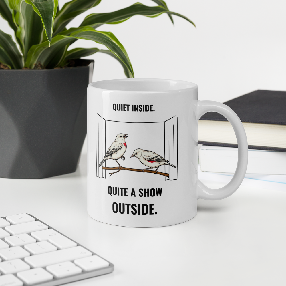 11 oz bird mug on a desk beside a plant and keyboard, showing QUIET INSIDE. QUITE A SHOW OUTSIDE. with two birds on a branch