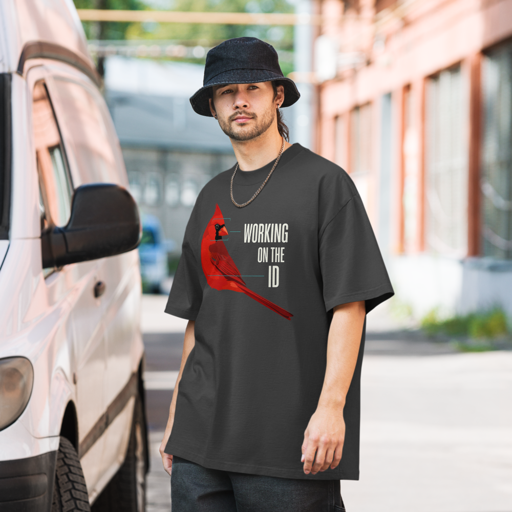 Man in the faded black bird nerd shirt on a city street, showing a cardinal with field-mark notes beside WORKING ON THE ID
