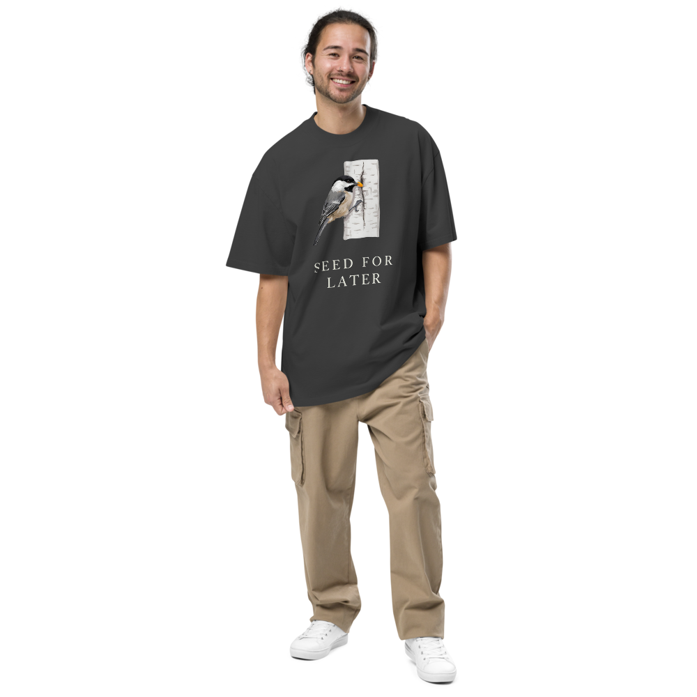 Man wearing the faded black bird t shirt with a chickadee tucking a seed into birch bark above SEED FOR LATER