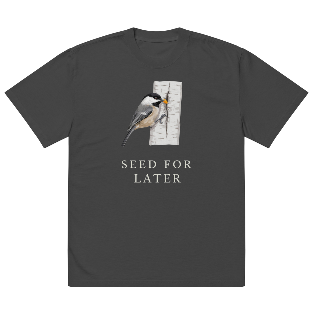 The faded black bird t shirt laid flat, showing a chickadee tucking a seed into birch bark above SEED FOR LATER