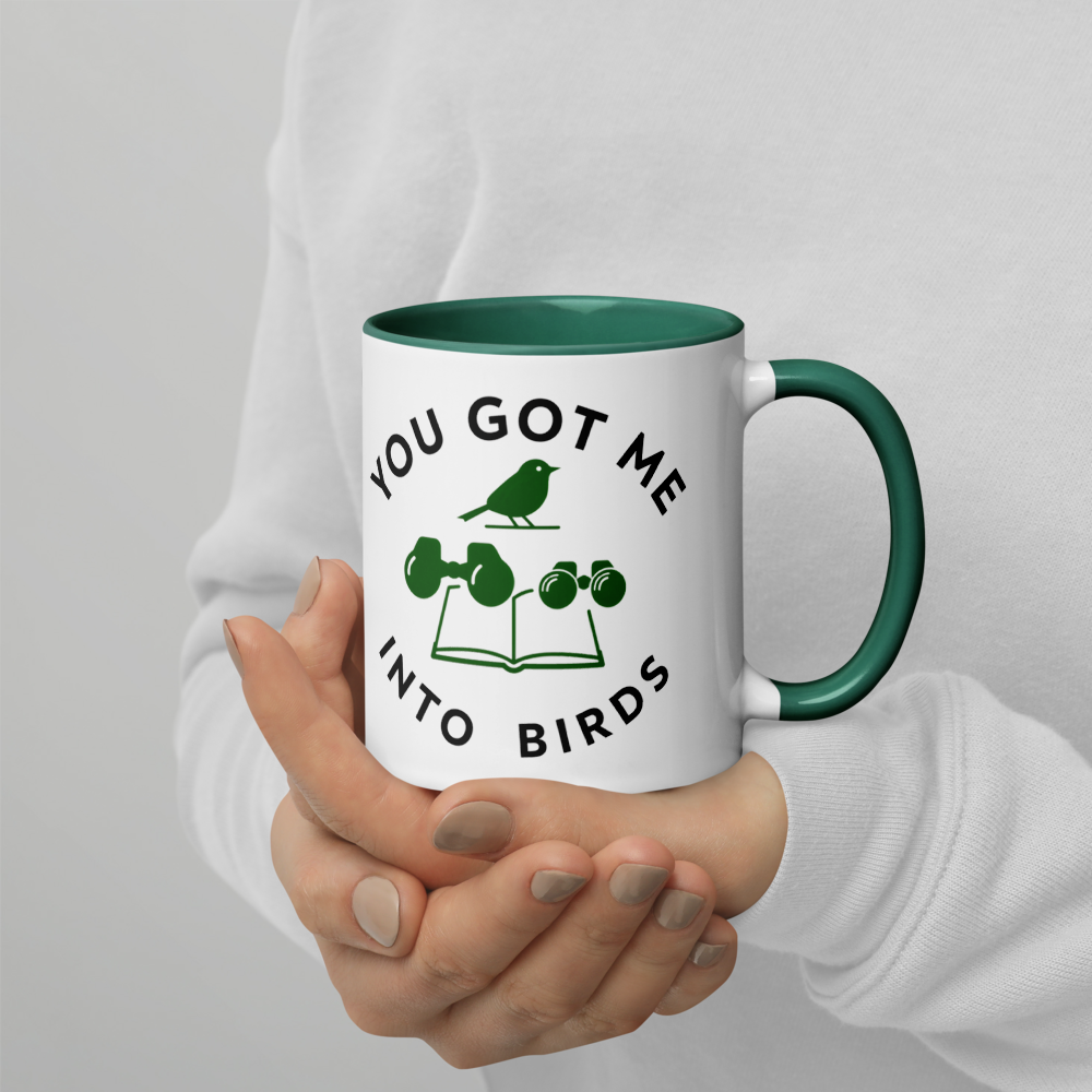 Hands holding the bird watcher gift mug with dark green inside, showing YOU GOT ME INTO BIRDS around a bird, binoculars and a field guide