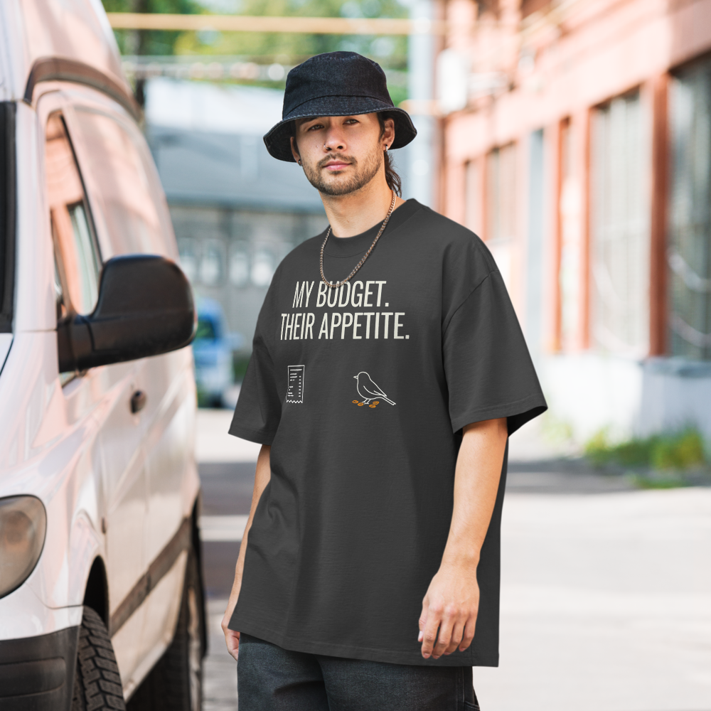 Man in the faded black bird watcher shirt on a city street, showing MY BUDGET. THEIR APPETITE. above a receipt and a pecking songbird