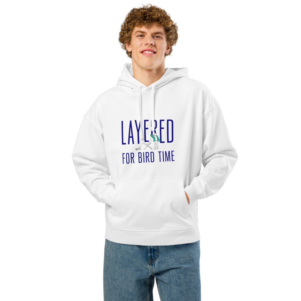 Man wearing the white bird watching hoodie with LAYERED FOR BIRD TIME with a watcher, a chair and binoculars