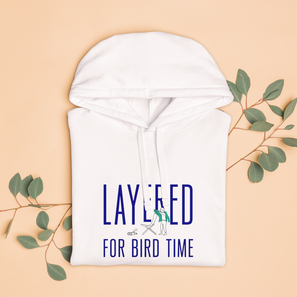 The white bird watching hoodie folded with eucalyptus leaves, showing LAYERED FOR BIRD TIME with a watcher, a chair and binoculars