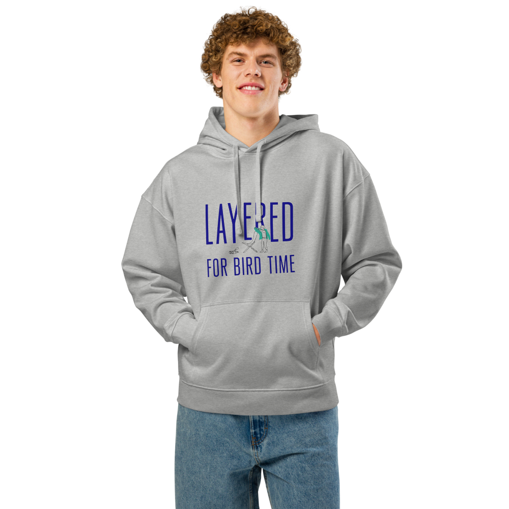 Man wearing the Heather Grey bird watching hoodie with LAYERED FOR BIRD TIME with a watcher, a chair and binoculars