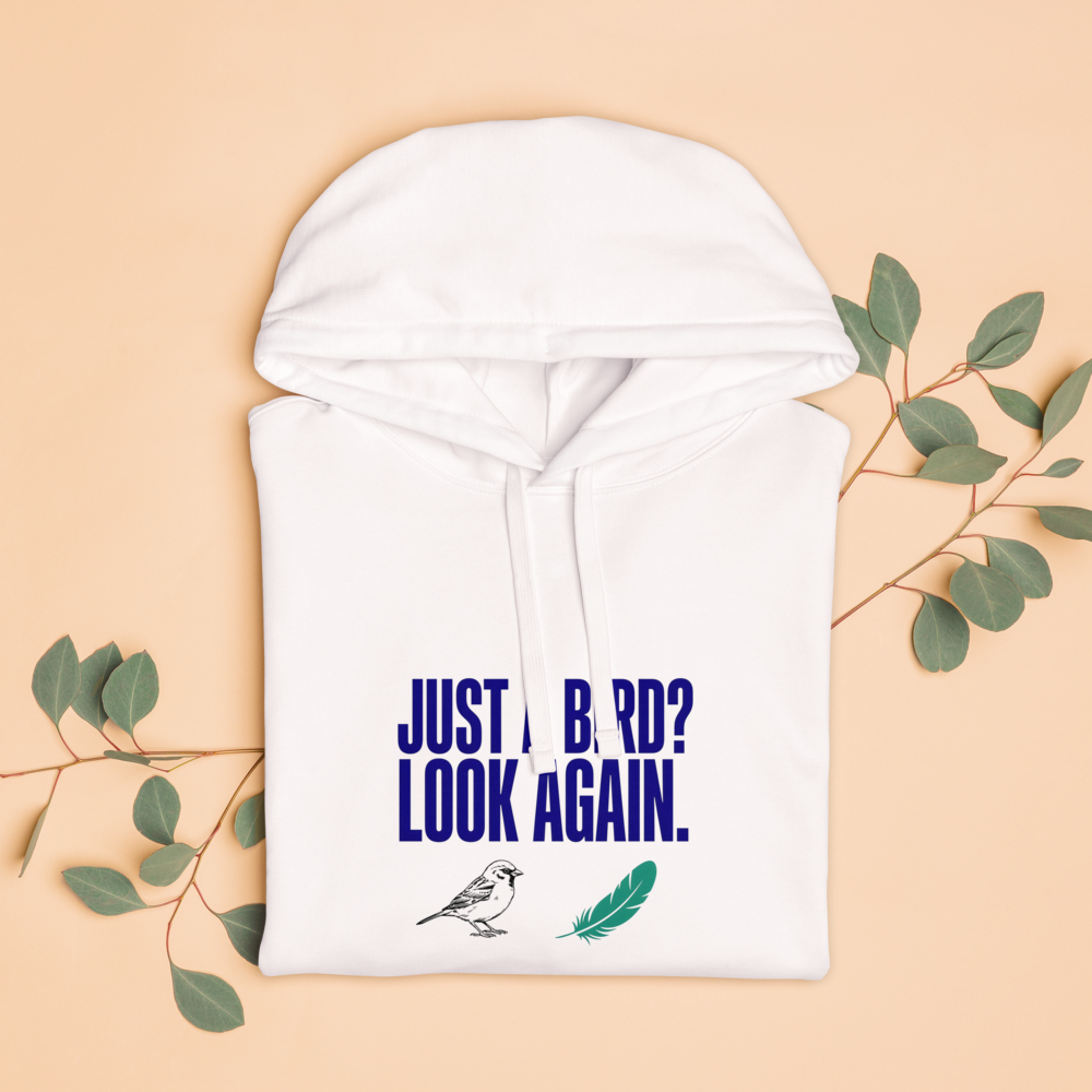The white birder hoodie folded with eucalyptus leaves, showing JUST A BIRD? LOOK AGAIN. above a sparrow and a feather