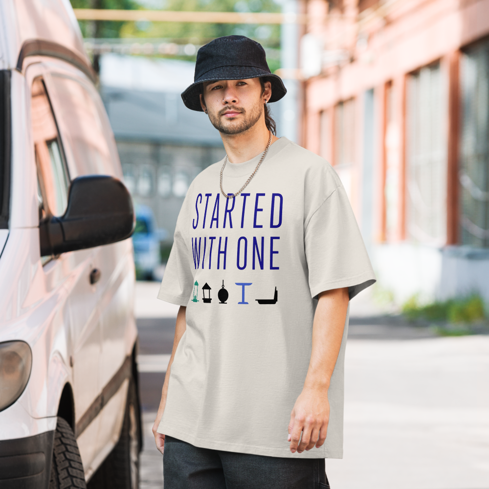 Man in the faded bone birding shirt on a city street, showing STARTED WITH ONE above a row of five bird feeders