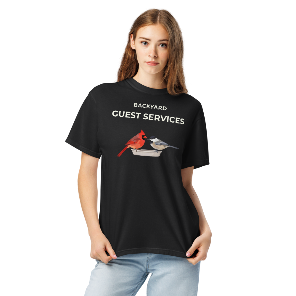 Close-up of a woman in the black cardinal shirt, showing BACKYARD GUEST SERVICES above a cardinal and a chickadee at a tray feeder
