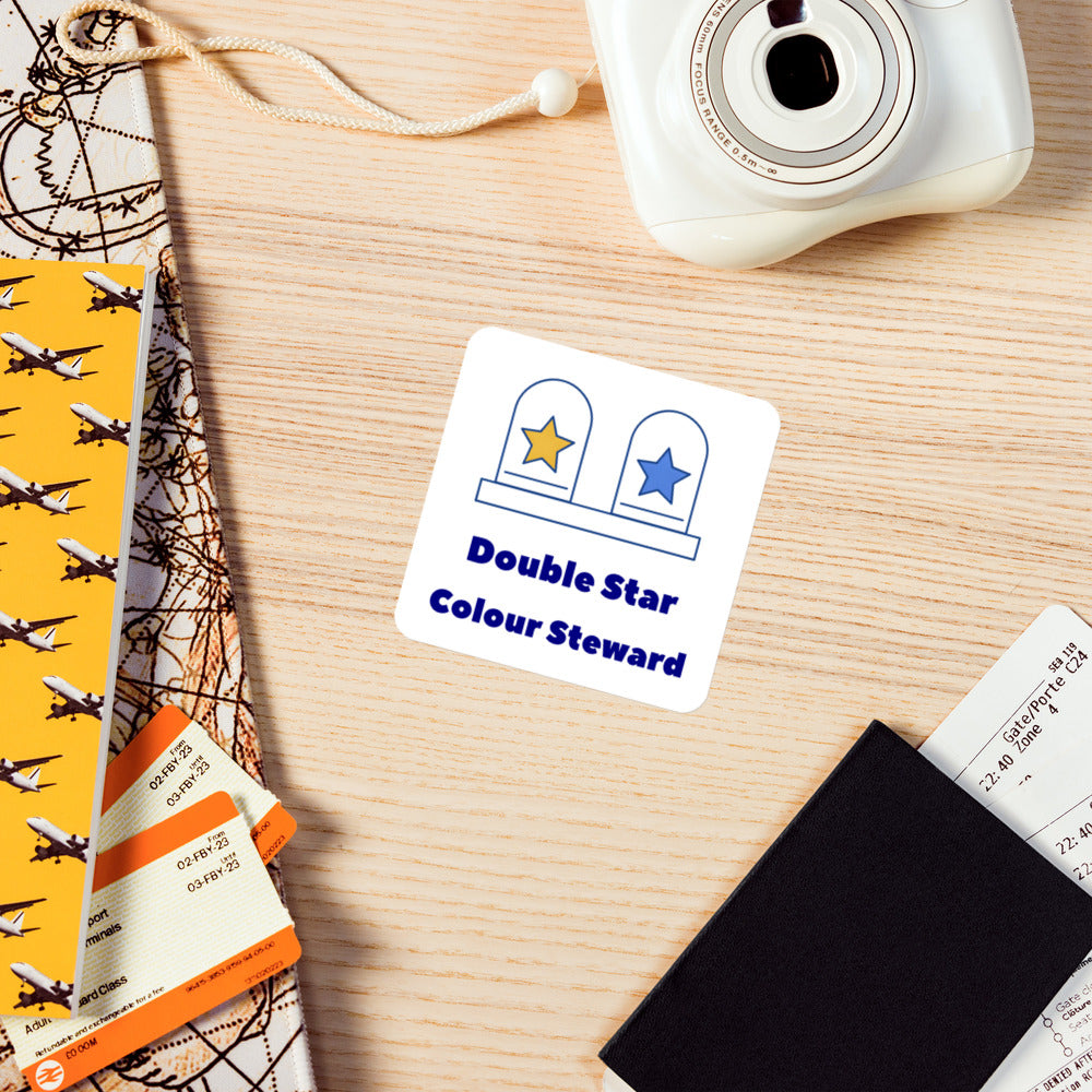 Double Star Colour Steward magnet on a wooden desk beside an instant camera and travel tickets