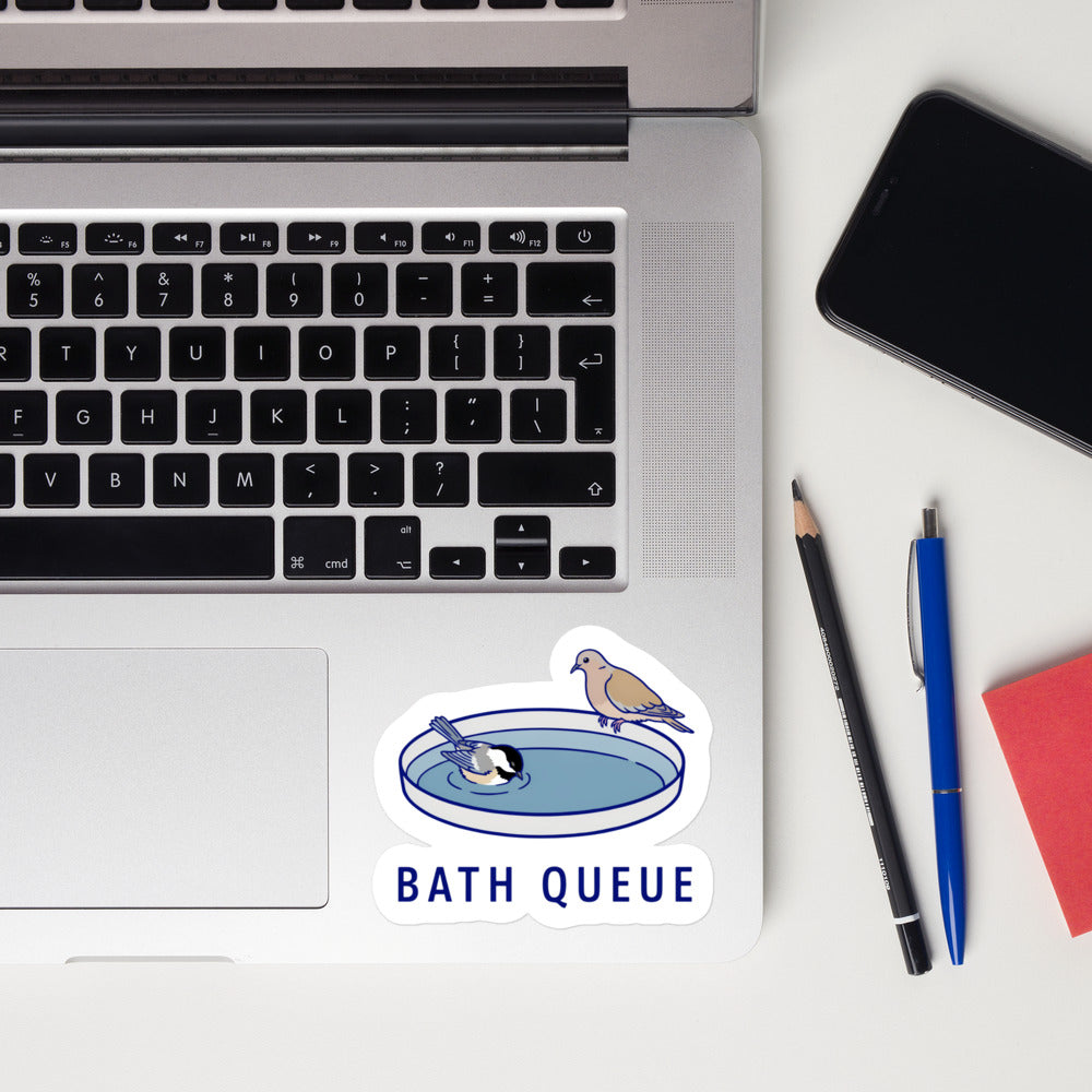 Bath Queue bird sticker on a laptop next to pens and a phone