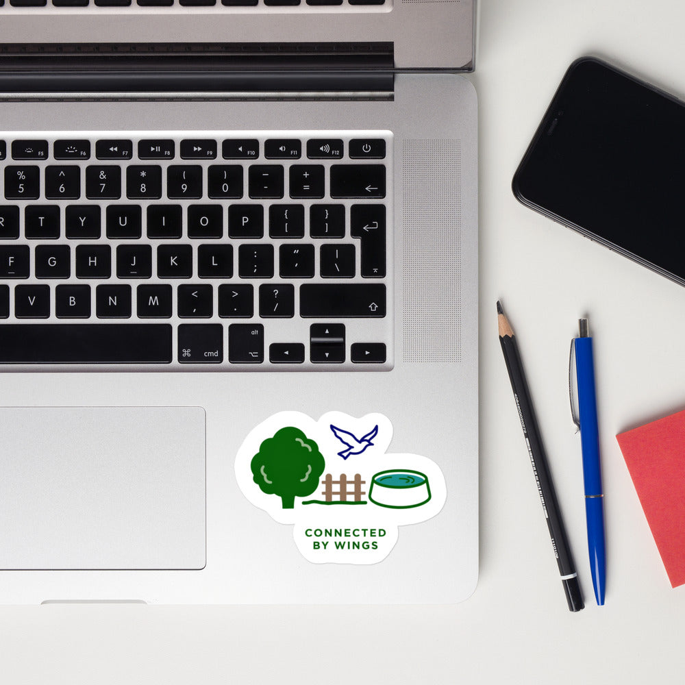 Connected by Wings bird lover sticker on a laptop next to pens and a phone