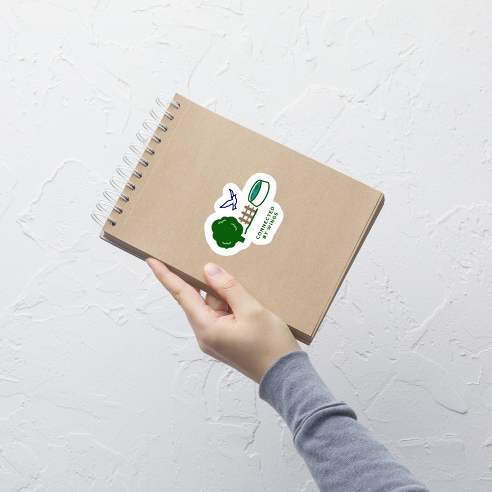 Hand holding a kraft notebook with the Connected by Wings bird lover sticker on the cover