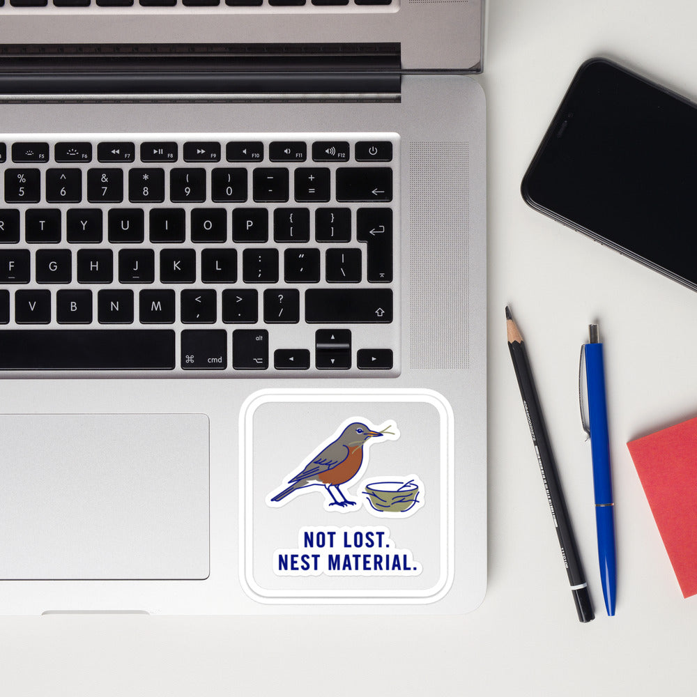 Not Lost. Nest Material. robin sticker on a laptop next to pens and a phone