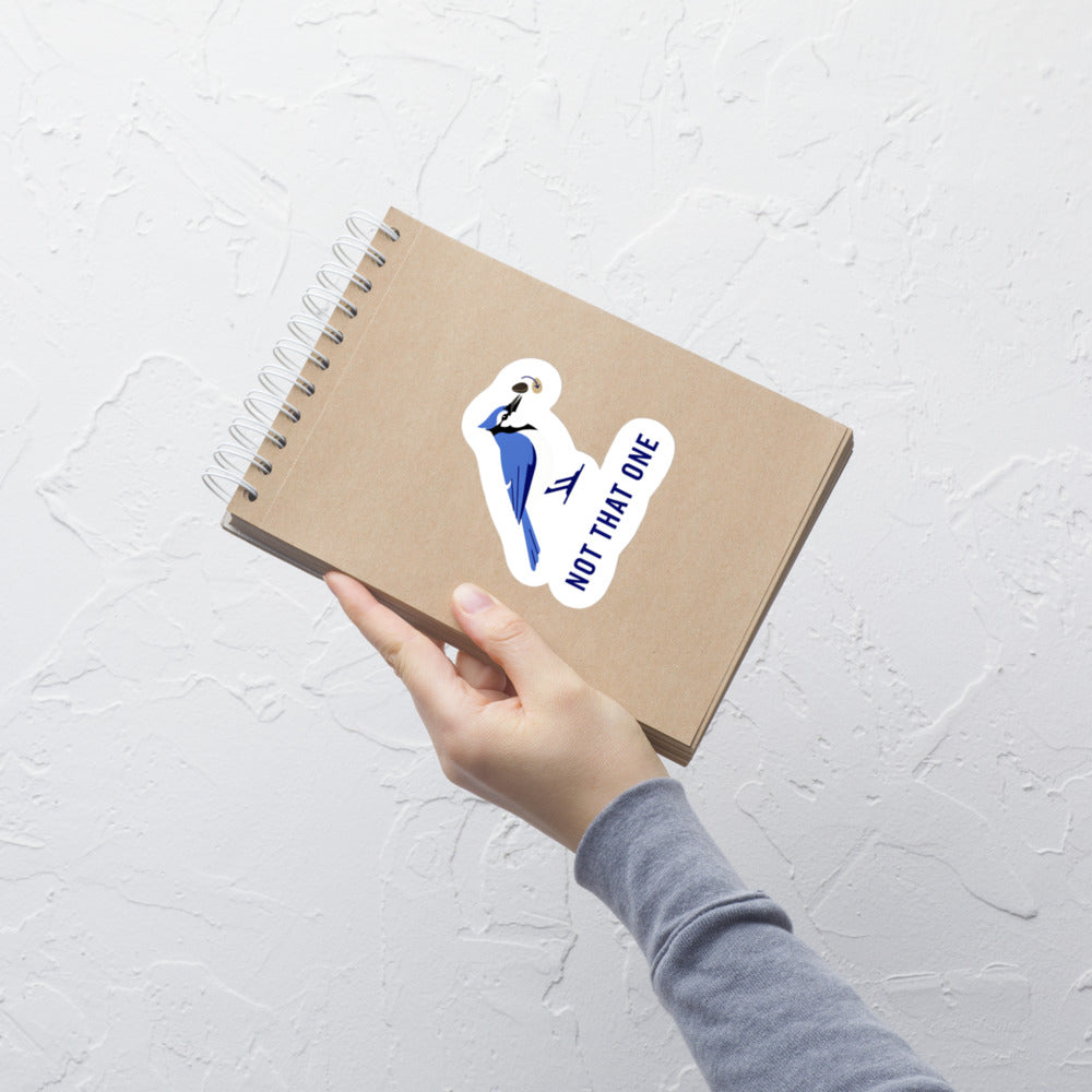 Hand holding a kraft notebook with the Not That One blue jay sticker on the cover