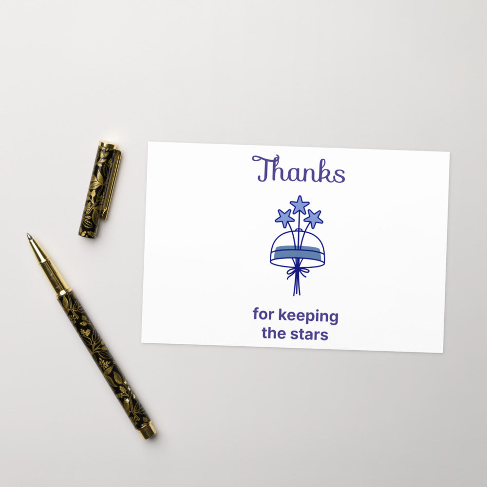 Dark sky thank you card, 4x6 in, reading Thanks for keeping the stars, on a pale desk beside a gold pen