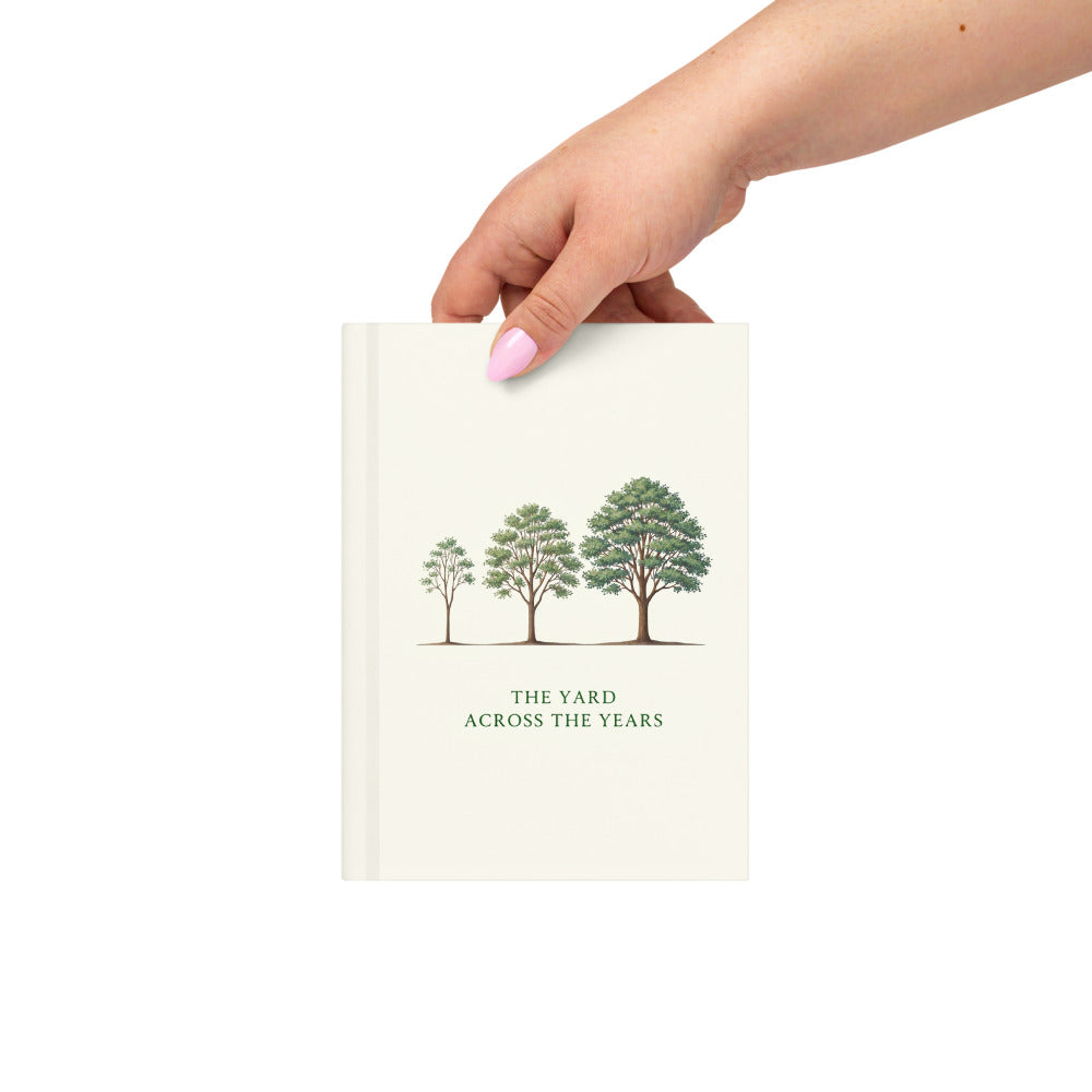 Hand holding the nature journal by its corner, with three green trees and deep-green lettering on the ivory front cover