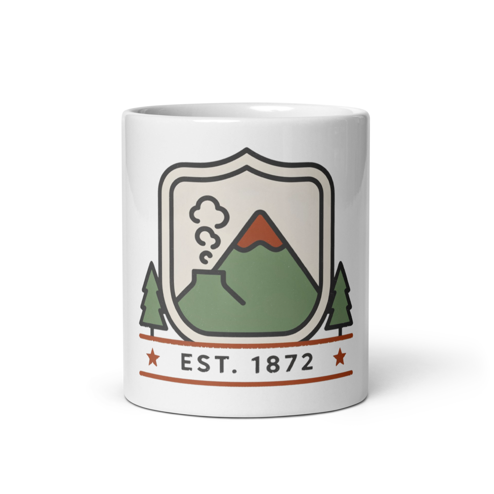 White glossy 11 oz ceramic mug printed with a shield badge of a steaming peak and pines above the wording Est. 1872