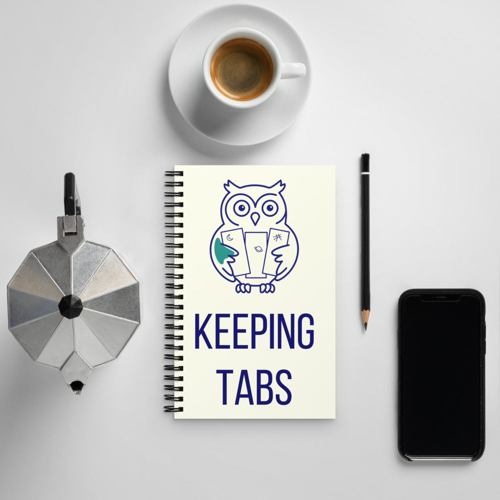 Keeping Tabs astronomy notebook with the navy owl cover on a white desk beside an espresso cup, moka pot, pencil and phone