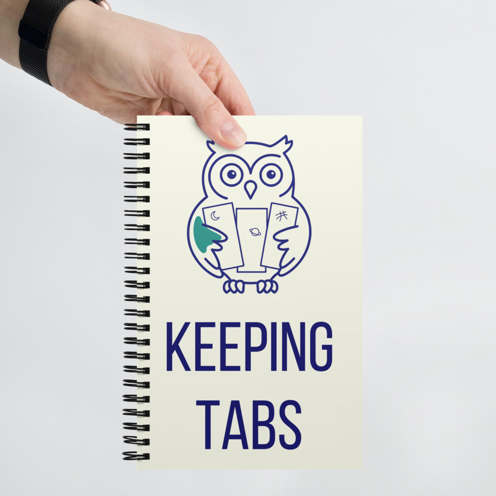 Hand holding up the Keeping Tabs astronomy notebook to show the owl and lettering on the ivory cover