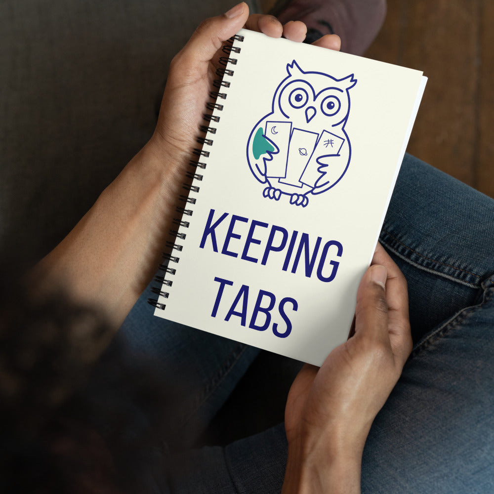 Stargazer holding the Keeping Tabs owl observing log on their lap, cover showing the owl with moon, planet and sketch-mark tabs