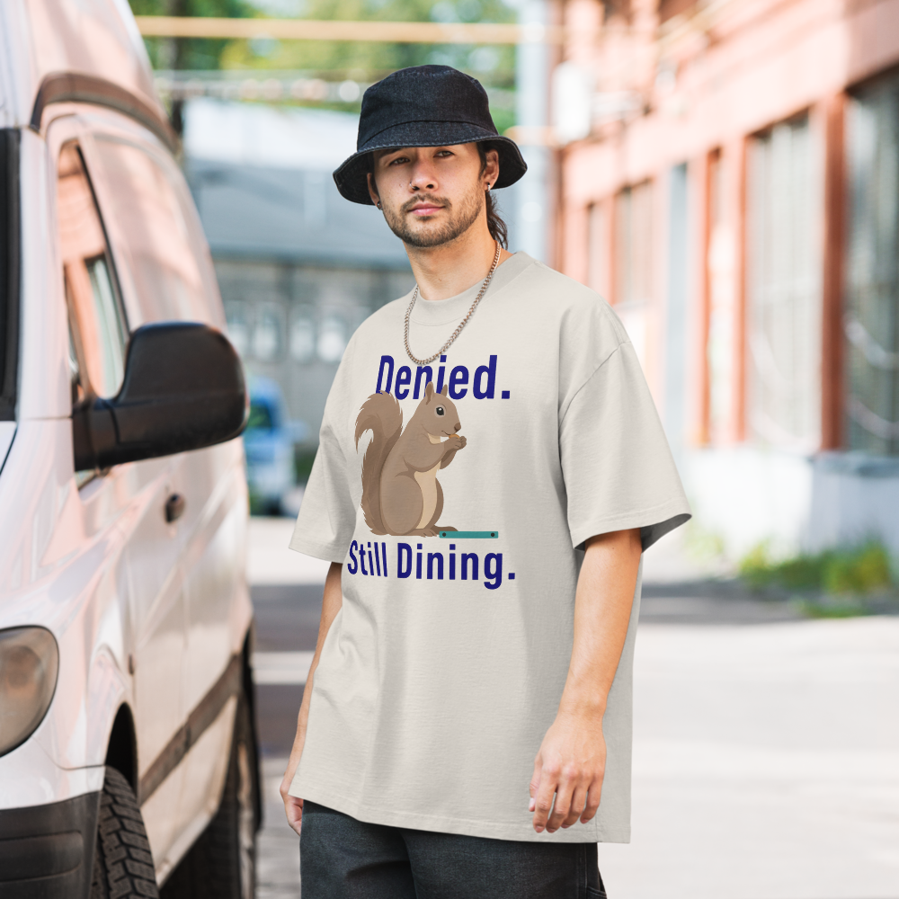 Man in the faded bone squirrel shirt on a city street, showing Denied. Still Dining. around a squirrel eating a seed
