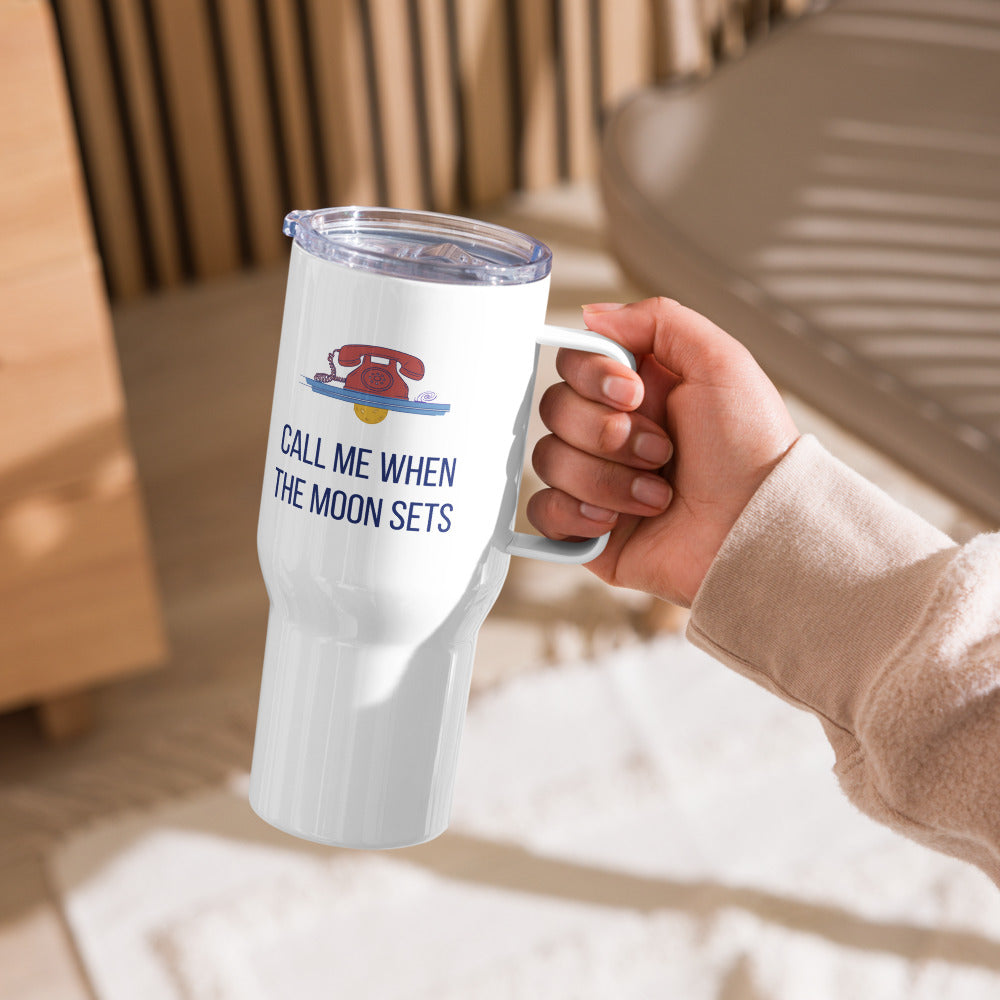 Hand holding the Call Me When the Moon Sets 25 oz travel mug by its handle, rotary phone and moon art facing out