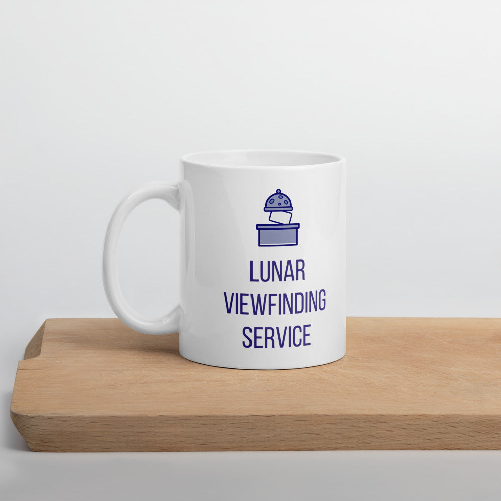 Lunar observer mug standing on a wooden board, crater-spotted dome and LUNAR VIEWFINDING SERVICE lettering facing out
