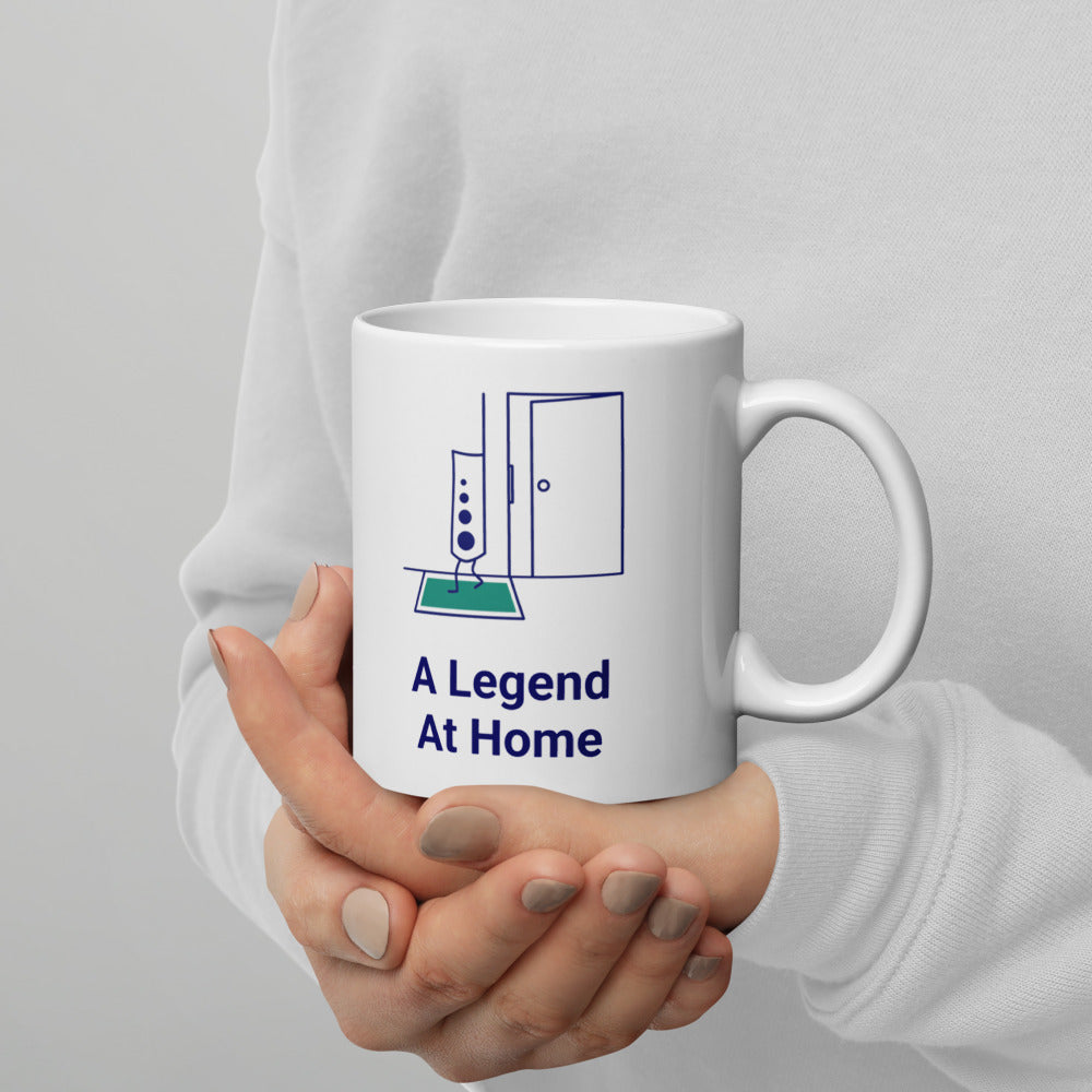 Hands in a white sweater cradling the 11 oz A Legend at Home mug, the open door and teal mat facing out