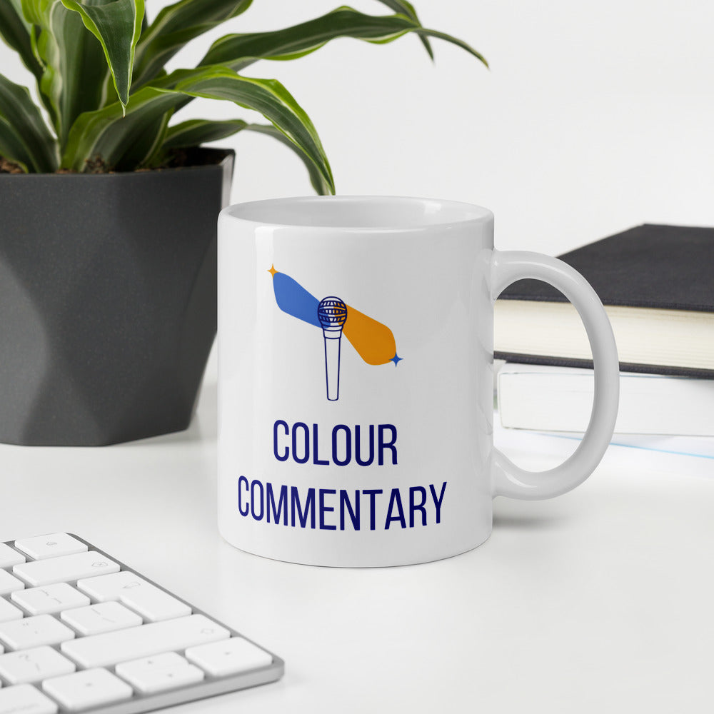 Colour Commentary astronomy mug on a white desk beside a keyboard, a plant and a stack of books