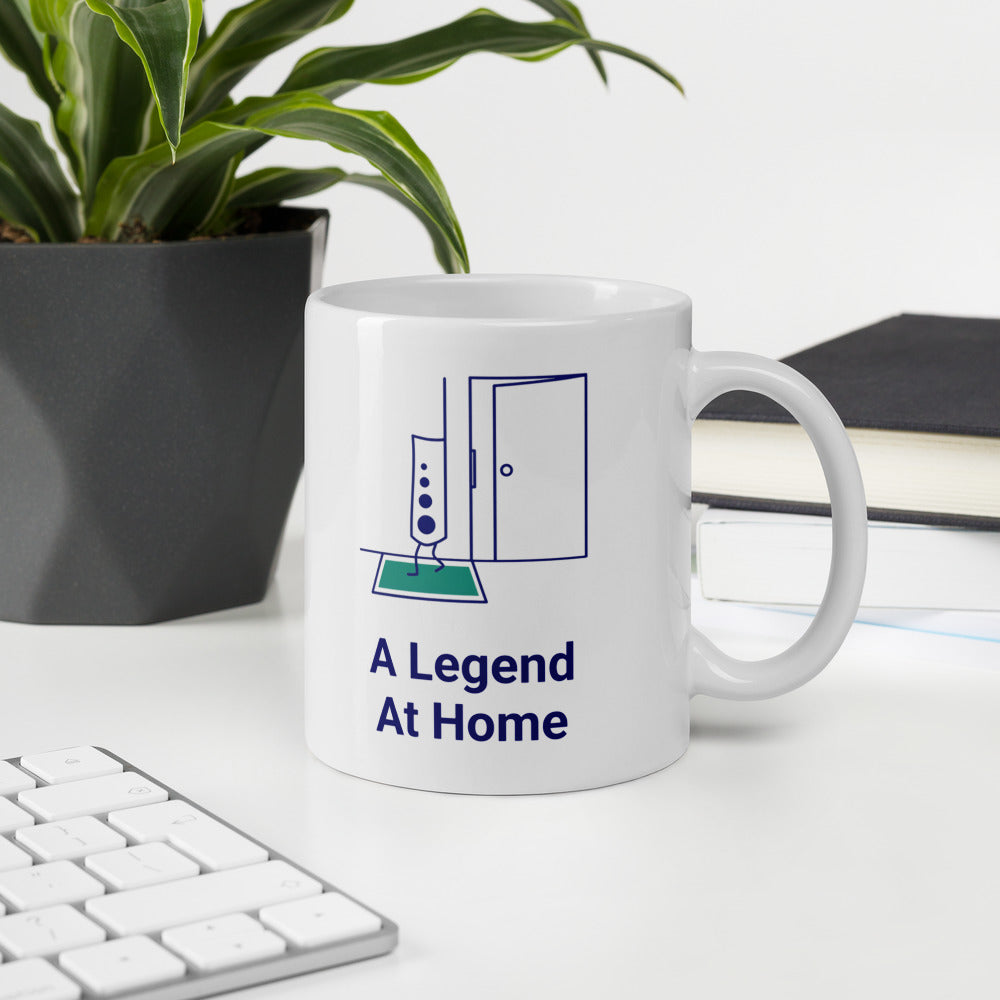 A Legend at Home astronomy mug on a white desk beside a keyboard, a plant and a stack of books